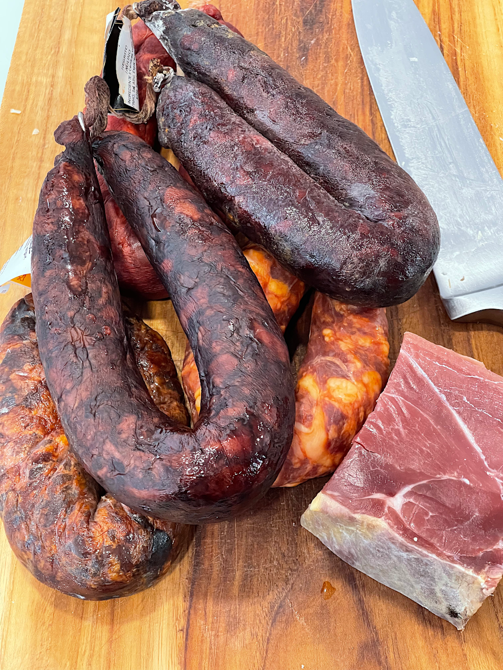 Os enchidos e o presunto sobre uma tábua: chouriços de carne e de sangue, morcela e negritos, e um naco de presunto, com uma faca ao lado