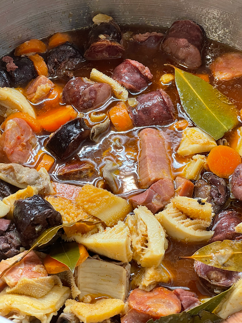 O tacho depois do refogado, com os enchidos, as carnes e o caldo já adicionado, e folhas de louro à superfície