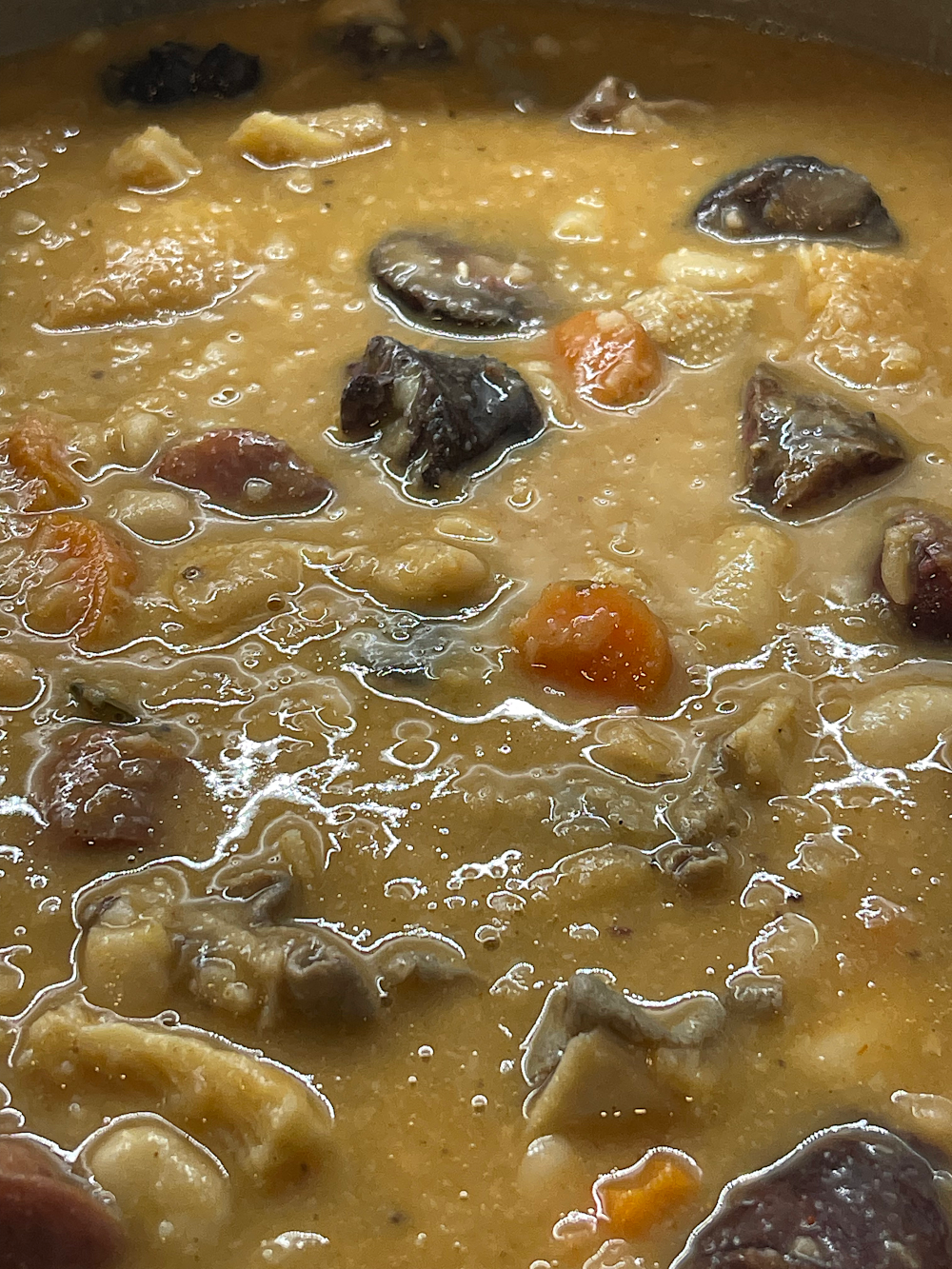 Pormenor do molho cremoso a apurar, com pedaços de cenoura, feijão e enchidos