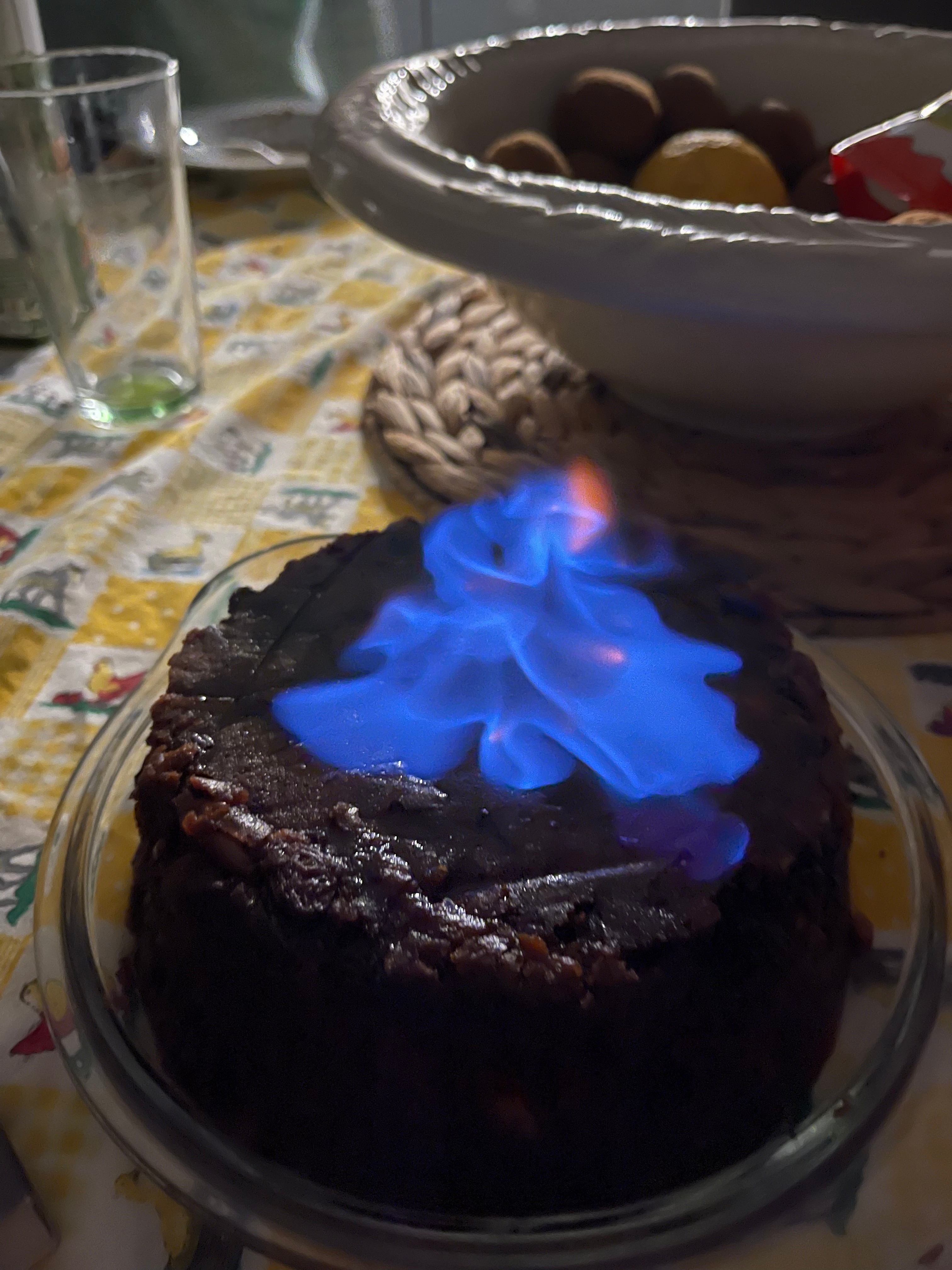 O bolo a flambar com chama azul sobre o prato, à mesa de Natal